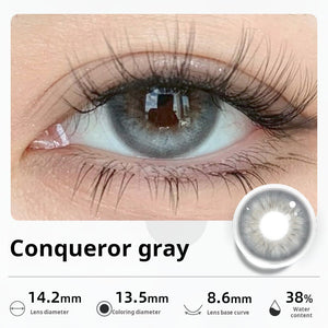 Close-up of an eye wearing "Conqueror gray" contact lenses, showing a striking, luminous light gray color. Specifications: 14.2mm diameter, 13.5mm graphic diameter, 8.6mm base curve, 38% water content.