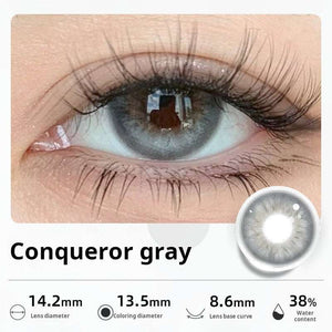 Close-up of an eye wearing "Conqueror gray" contact lenses, showing a striking, luminous light gray color. Specifications: 14.2mm diameter, 13.5mm graphic diameter, 8.6mm base curve, 38% water content.