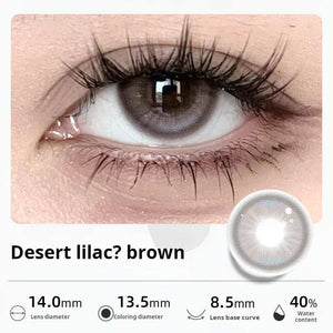 Close-up of an eye wearing "Desert lilac? brown" contact lenses, showing a unique blend of muted purple and brown tones. Specifications: 14.0mm diameter, 13.5mm graphic diameter, 8.5mm base curve, 40% water content.