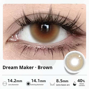 Close-up of an eye wearing "Dream Maker - Brown" contact lenses, featuring a warm hazel-brown center. Specifications: 14.2mm diameter, 14.1mm graphic diameter, 8.5mm base curve, 40% water content.