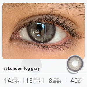 Close-up of an eye wearing "London fog gray" contact lenses, displaying a soft, misty gray shade. Specifications: 14.2mm diameter, 13.1mm graphic diameter, 8.5mm base curve, 40% water content.