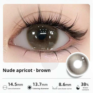 Close-up of an eye wearing "Nude apricot - brown" contact lenses, showing a soft, natural dark brown tint. Specifications: 14.5mm diameter, 13.7mm graphic diameter, 8.6mm base curve, 38% water content.