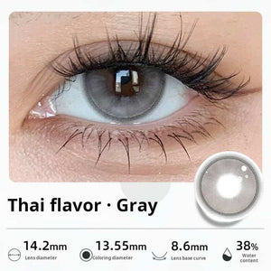 Close-up of an eye wearing "Thai flavor - Gray" contact lenses, showing a light gray hue with soft gradients. Specifications: 14.2mm diameter, 13.55mm graphic diameter, 8.6mm base curve, 38% water content.