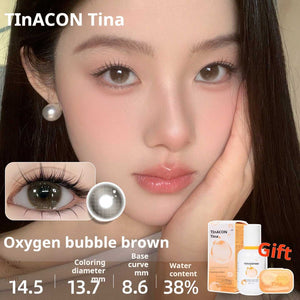 Close-up of an eye wearing Oxygen bubble brown lenses, displaying a natural warm brown hue. Specs: 14.5mm diameter, 13.7mm graphic diameter, 8.6mm base curve, 38% water content.