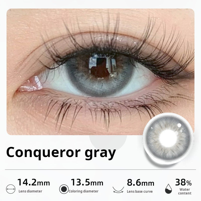 Close-up of an eye wearing "Conqueror gray" contact lenses, showing a striking, luminous light gray color. Specifications: 14.2mm diameter, 13.5mm graphic diameter, 8.6mm base curve, 38% water content.