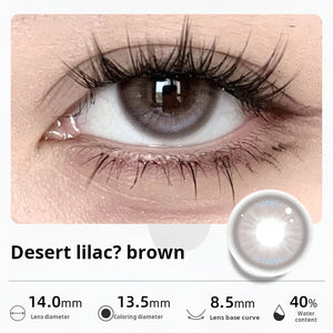 Close-up of an eye wearing "Desert lilac? brown" contact lenses, showing a unique blend of muted purple and brown tones. Specifications: 14.0mm diameter, 13.5mm graphic diameter, 8.5mm base curve, 40% water content.