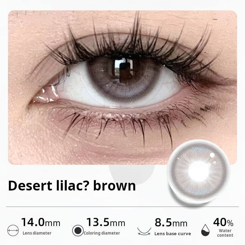 Close-up of an eye wearing "Desert lilac? brown" contact lenses, showing a unique blend of muted purple and brown tones. Specifications: 14.0mm diameter, 13.5mm graphic diameter, 8.5mm base curve, 40% water content.