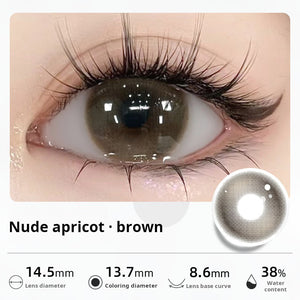 Close-up of an eye wearing "Nude apricot - brown" contact lenses, showing a soft, natural dark brown tint. Specifications: 14.5mm diameter, 13.7mm graphic diameter, 8.6mm base curve, 38% water content.
