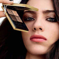 Close-up of a woman holding YSL Couture Color Eyeshadow palette with warm and neutral shades near her eye